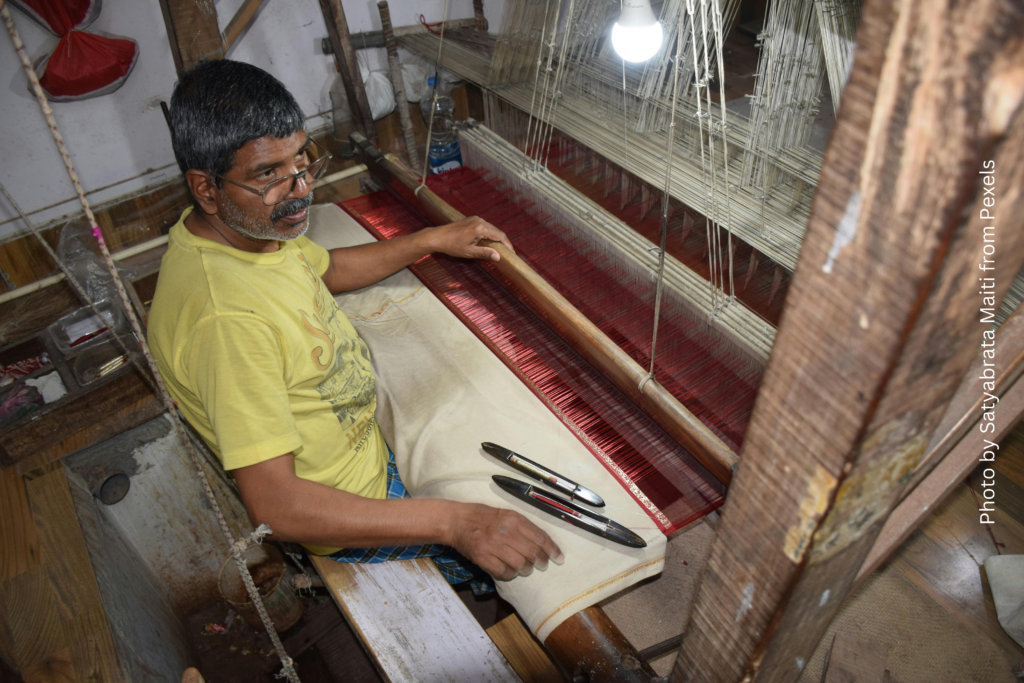 A man weaving on a traditional loom, surrounded by colorful threads and fabric